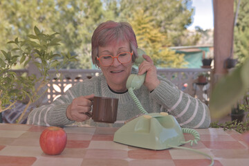 Mujer mayor con gafas llamando con un teléfono de disco antiguo de color verde