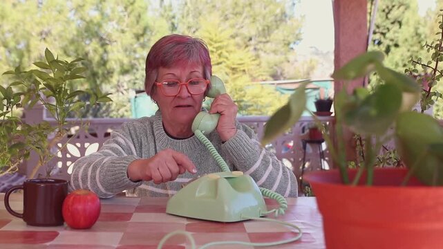 Mujer mayor con gafas llamando con un tel&eacute;fono de disco antiguo de color verde