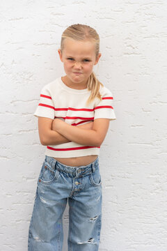 young girl with grumpy facial expression and arms crossed, wearing striped shirt and blue jeans