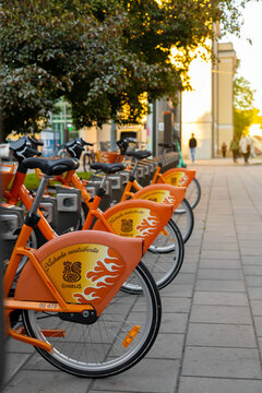 Vilnius, Lithuania - September 23 2025: Bright orange Cyclocity Vilnius rental bikes with Gaidelis branding lined up at a docking station at sunset in warm golden evening light