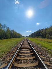 Obraz premium Railway tracks leading to horizon under bright sun in rural landscape