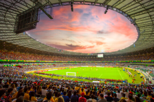 Blurred view of a crowded soccer stadium at sunset, out of focus background for sports advertising and social media.