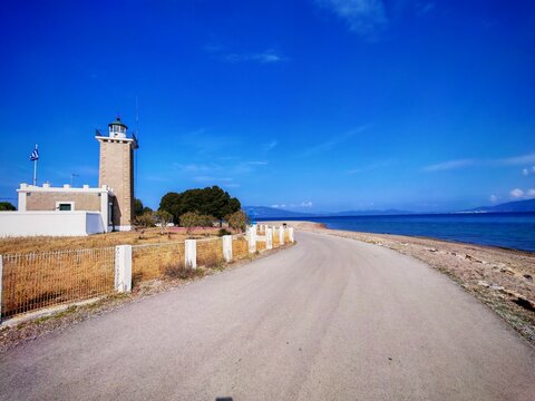Historic lighthouse of Arkitsa on the coast of mainland Greece, a winding road leading along the beach and the deep blue waters of the Euboean Gulf, with the Evia island in background