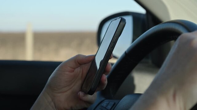 Driver texting on smartphone while holding steering wheel for distracted driving and road safety, mobile phone use and accident risk or traffic awareness concept.