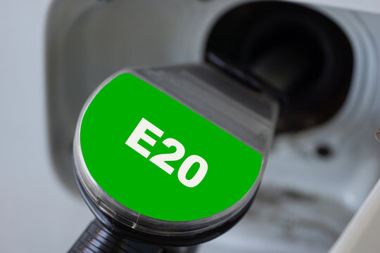 green fuel nozzle with e20 label inserted into a car gas tank, close up of fueling a vehicle at a gas station, eco friendly ethanol gasoline blend, concept of ecology, automotive, transport