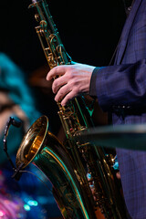 Obraz premium Mans Hands Holding a Saxophone on Stage with a Performer in the Background on Stage