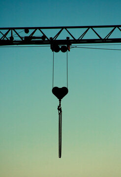 Close-up silhouette of a crane jib with a heart shaped pulley at sunset