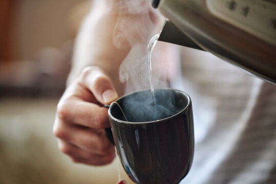 Pouring hot water from kettle into steaming cup
