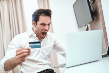 Fototapeta premium Man screaming holding credit card facing laptop