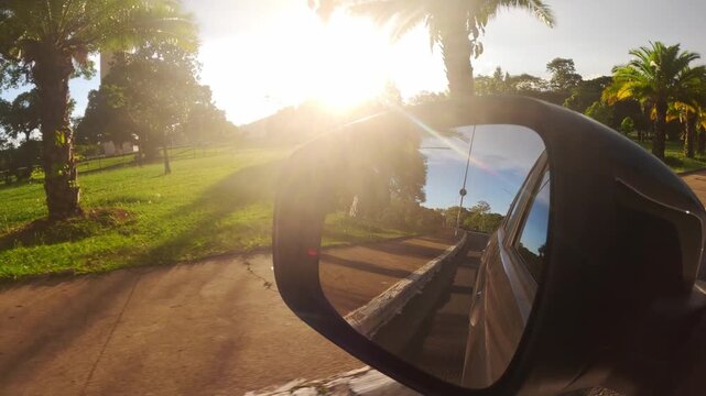View from a car of Ibirapuera Park in Sao Paulo, at sunset. The Obelisk monument is in the background, and the road is reflected in the side mirror.