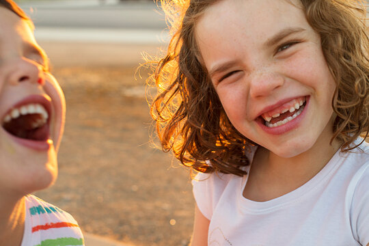Close-up portrait of two happy children standing in a garden at sunset laughing