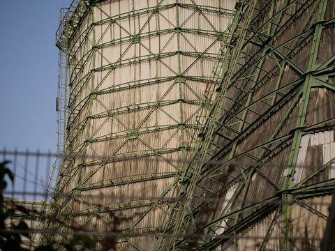 Industrial cooling towers with green steel framework and weathered wood paneling under a blue sky. Detailed view of massive power plant infrastructure, engineering architecture, and heavy industry fac