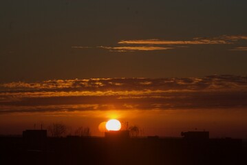 Obraz premium Golden hour sun setting behind urban horizon with expressive clouds.