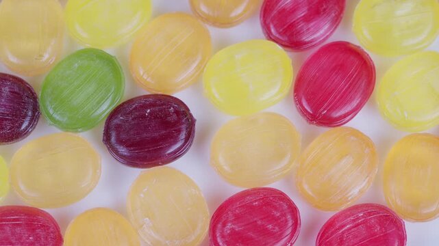Vivid candy display. Multicolored spherical sweets arranged on plain backdrop for display. Assorted vibrant candies spread across white background with glossy sugar coating
