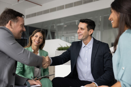 Two diverse male colleagues celebrating teamwork success with handshake on informal staff meeting in office showing mutual respect trusted partnership making agreement after professional networking