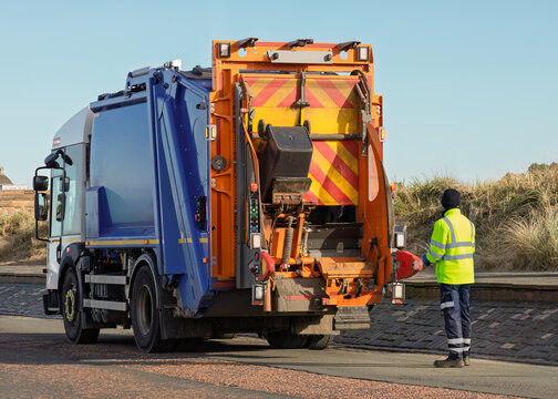 Sanitation worker operating refuse collection truck during waste pickup