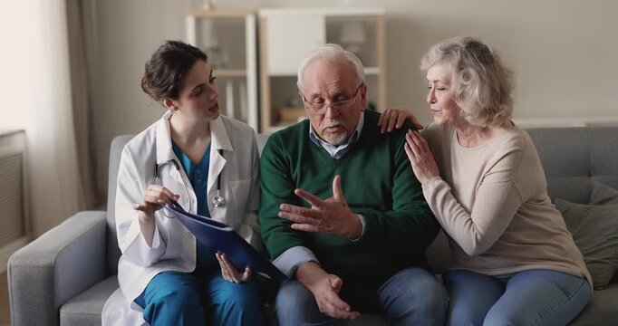 Doctor explaining diagnosis or medical results on clipboard to senior 70s retired couple, reviewing together treatment plan, giving professional recommendations during visit. Health care consultation