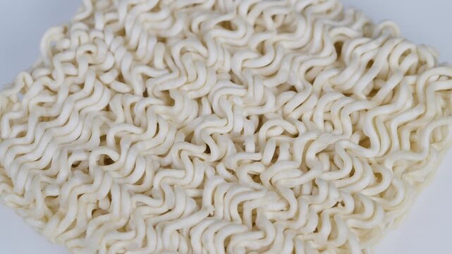 Closeup dry instant noodles block showing tight curly texture, pale wheat tone, dense repeating pattern on white background, studio food styling for packaging photography