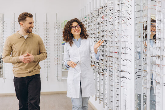 Smiling optician showing new eyewear to a happy male client in a modern optical shop for vision care and eye health