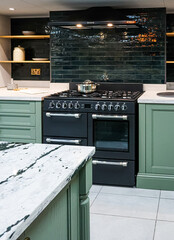 Contemporary kitchen interior featuring dark green metro tiles, a black range cooker, and a white...