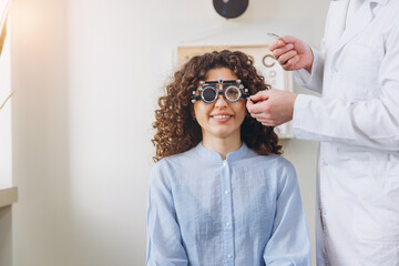 Patient receiving an eye exam, sitting in a chair while an optometrist adjusts a trial frame for...