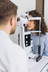 Patient having an eye examination with optometrist using a slit lamp for vision checkup and...