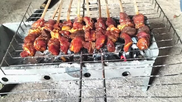 The process of grilling goat satay, a traditional Indonesian dish made from tender goat meat, over hot charcoal produces smoke and flames that enhance the flavor. Footage.