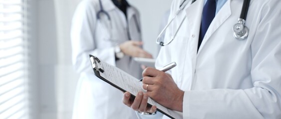 Doctor taking notes on clipboard during discussion with medical team involved in collaborative...