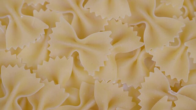 Dense arrangement of uncooked bowtie pasta with rustic container background. Detailed image showing overlapping uncooked bowtie pasta with textured edges and rustic environment