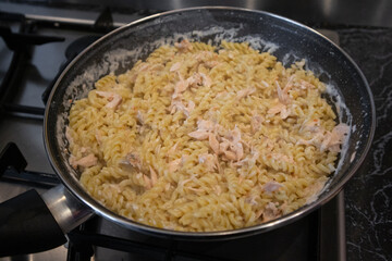 Creamy pasta fusilli with salmon pieces in a frying pan on a kitchen stove