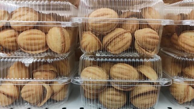 Rows of Oreshki cookies with boiled condensed milk filling displayed in transparent boxes. Large stock of popular Eastern European desserts in supermarket bakery area. Sweet walnut-shaped pastries 