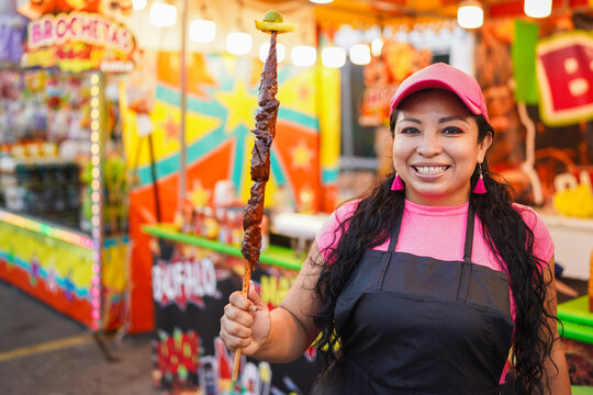 Latin woman entrepreneur smiling holding meat skewer