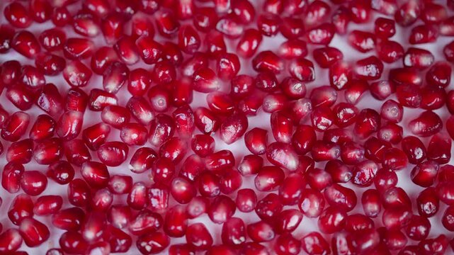 Vivid fruit closeup. Juicy ruby seeds on surface. Shiny pomegranate arils glittering vividly closeup. Detailed view of glossy red pomegranate seeds on white background