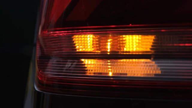 Rear car taillight with blinking amber turn signal, close up automotive lighting detail, safety indication, modern vehicle design, night visibility, transportation technology feature system