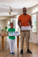 African American father and son holding clear recycling bins labeled GLASS and PAPER at home entry