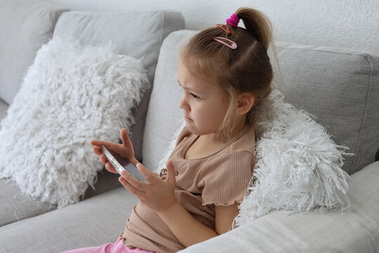 Little girl using smartphone while sitting on couch at home