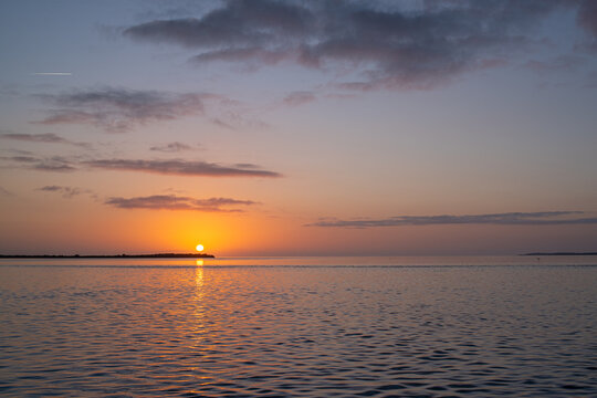 Orange sunrise over a calm ocean with an island and clouds in the sky