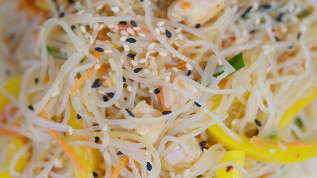 Closeup rice vermicelli salad with sesame seeds, shredded chicken, julienned yellow pepper, grated carrot, chopped scallion, light soy dressing, bright fresh streetfood styling