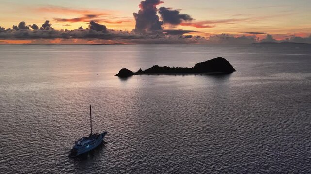 A serene sunrise silhouettes a small island in the Vatu-i-ra seascape in Fiji. This area is a marine protected area known for its high biodiversity and is a destination for divers and snorkelers.