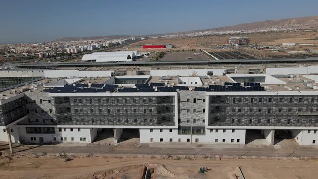 Vue a&eacute;rienne par drone d'un grand b&acirc;timent moderne et d'une infrastructure en construction avec des panneaux solaires sur le toit &agrave; Agadir, Maroc.