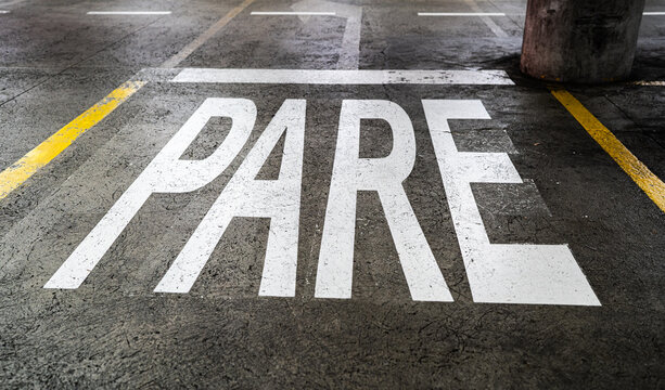 Se&ntilde;al de &ldquo;PARE&rdquo; pintada en el pavimento de un estacionamiento urbano