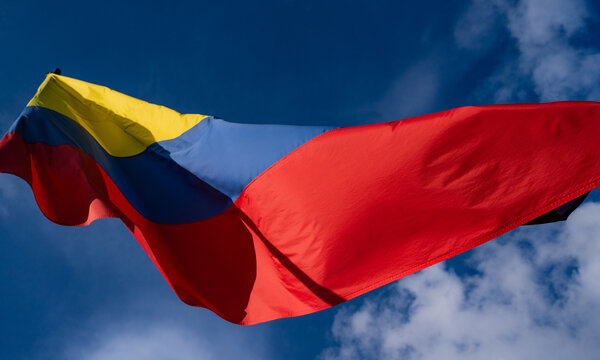Bandera de Colombia ondeando al viento contra un cielo azul con nubes