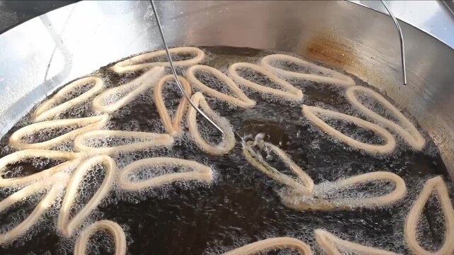  flipping churros while frying in boiling oil using metal rods inside a professional fryer. Essential equipment in traditional Spanish churrer&iacute;as