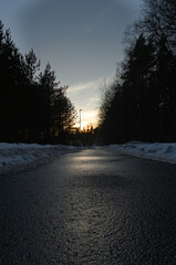 Reflective Sunset Roadway. Calm Twilight Scene Featuring Shimmering Asphalt And Silhouetted Trees