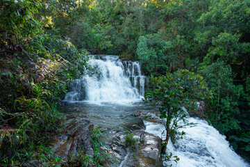 Obraz premium Waterfall cascading over multi-tiered rocky formations surrounded by lush green tropical forest, expressing the power of water, natural beauty, and untouched wilderness