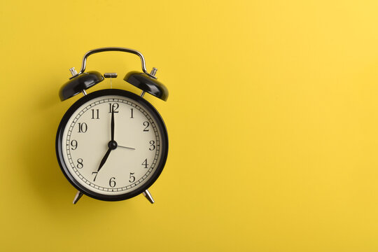 Classic black alarm clock set at seven o'clock isolated on a yellow background