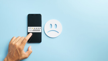 Experience poor customer service, hand inputs negative online review on mobile phone, displaying one star feedback rating for low satisfaction, with prominent unhappy face