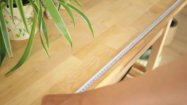 Hand holding measuring tape, taking measurements on wooden surface, close-up shot