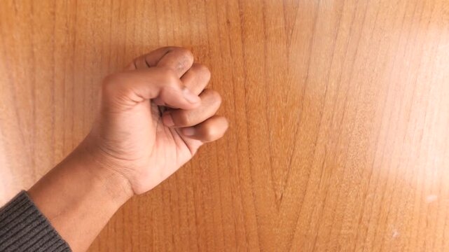 Person knocking on wooden door surface using fist to get attention from behind closed room entrance