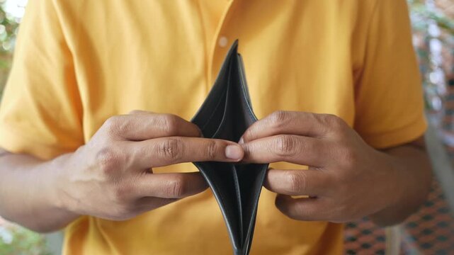 Close up of man in yellow shirt showing empty brown wallet to camera showing no money